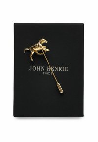 Gul hästsksjortsnål på en smal metallstam presenterad på ett svart kort med "JOHN HENRIC SWEDEN" i silverfärgade bokstäver.
