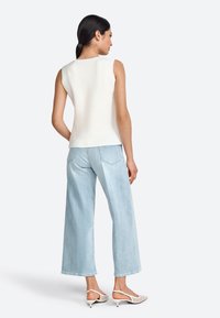 Top blanco sin mangas con un acabado texturizado, combinado con jeans de pierna ancha de color azul claro. Modelo con zapatos de tacón en beige.