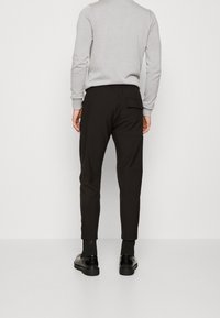 Svart slim-fit byxor med elastisk midja, sidofickor och bakficka. Matchas med en ljusgrå långärmad skjorta och svarta skor.