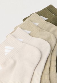 Öt pár sportzokni különböző bézs és zöld árnyalatokban, bordázott textúrával, fehér háromszög alakú díszítéssel a szegély közelében.