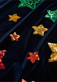 Tissu en velours noir orné de sequins en forme d'étoile multicolores vert, or, rouge et orange, créant un design texturé.