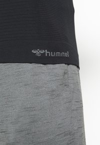 Close-up of black textured fabric top with grey "hummel" logo above heather grey pants pocket.