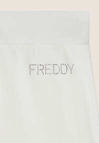 Tela blanca con una textura suave presenta la palabra "FREDDY" en pequeños strass brillantes, centrada hacia la parte inferior.