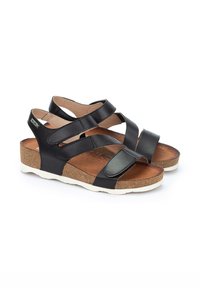 Sandalias de cuero negro con correas entrelazadas, plantilla de corcho y suela blanca. El diseño presenta una textura suave y un ligero brillo.