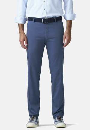 Homme portant une chemise bleu clair boutonnée avec les manches retroussées, une ceinture tissée bleu marine, un pantalon bleu et des baskets bleu et blanc.