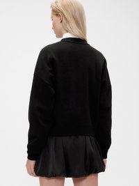 Sweat-shirt noir avec une coupe décontractée et un col rond, associé à une jupe noire volumineuse. Texture lisse et design minimal.