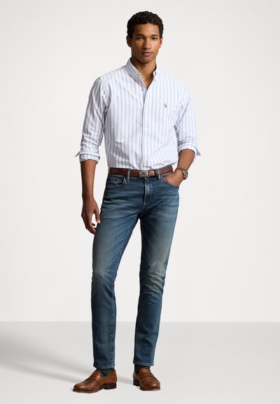 Light blue and white striped button-up shirt, dark blue jeans, brown leather shoes, and a brown belt. Features a small logo on the shirt.