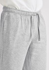 Grå joggingbukser lavet af blødt stof med en elastisk talje og snøre samt sidelommer. Glat tekstur og afslappet pasform.