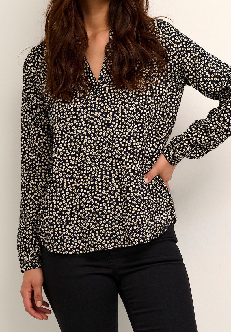 Blouse à manches longues en bleu marine foncé avec un motif floral crème, dotée d'un col en V et d'une coupe décontractée. Tissu lisse et léger ; léger éclat.