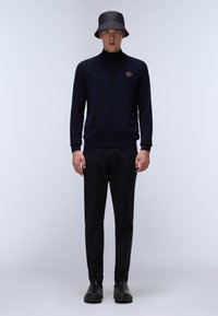 Marinblå zip-up tröja med texturerad design, kombinerad med svarta byxor och en svart bucket hat med en logotyp. Enfärgade, avslappnad passform.