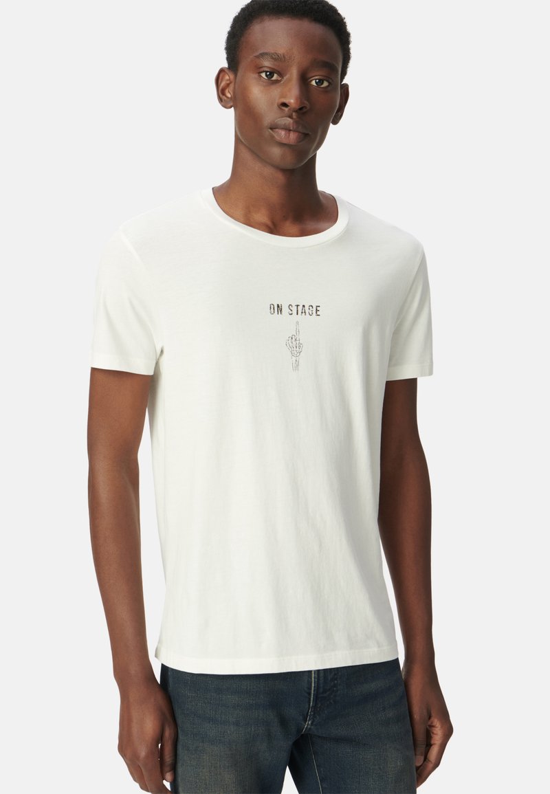 Camiseta blanca de algodón con mangas cortas, que presenta un texto gráfico "EN ESCENA" y una ilustración de una mano en el centro. Diseño clásico de cuello redondo.