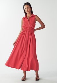 Korala, bezrękawna sukienka na guziki z elastycznym pasem, zwiewnym dołem i kołnierzykiem. Gładki materiał, luźny krój.