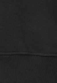 Svart bomullssweatshirtmaterial med ribbat mönster och nederkant. Slät yta med subtila sömdetaljer längs kanterna.