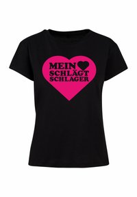 Sort bomulds T-shirt med korte ærmer, der har et stort pink hjertegrafik og fed sort tekst, der står "MEIN ♥ SCHLÄGT SCHLAGER."