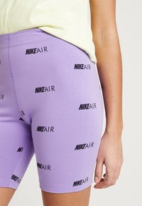 Lila cykelshorts i stretchigt material, med upprepade svarta "NIKE AIR"-logotyper i ett enhetligt mönster. Slim fit och mediummidtalsdesign.