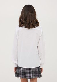 Blusa bianca a maniche lunghe con colletto con bottoni, abbinata a una gonna plissettata a quadri nera con accenti rosa. Tessuto morbido.
