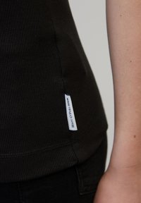 Must mustriba tank top, mille väikese valge sildiga, millel on sinine tekst külje peal. Kangas näeb välja veniv ja sobib selga.