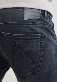 Mörk denimjeans med en strukturerad tyg, synliga sömmar och en läderlapp märkt "CHASIN'" på bakre midjan.