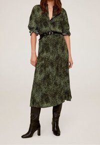 Abito midi a stampa serpente verde con colletto, maniche lunghe e vita con cintura, abbinato a stivali neri con tacco al ginocchio.