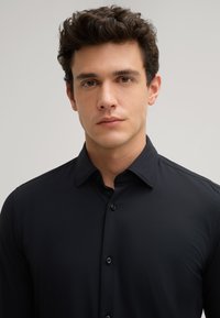 Schwarzes Button-Up-Hemd aus glattem, leichtem Stoff mit standardmäßigem Kragen, mit einer Knopfleiste vorne und subtiler glänzender Oberfläche.