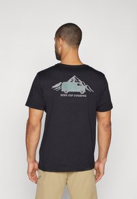 Black cotton t-shirt featuring a graphic of a van and mountains on the back, with the text "NEVER STOP EXPLORING" beneath the design.