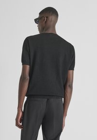 Maglione lavorato a maglia nero a maniche corte con texture a coste, caratterizzato da un collo rotondo e una vestibilità comoda, abbinato a pantaloni neri.