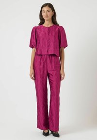 Fuksjowy dwuczęściowy zestaw z teksturowanym wzorem fal. Krótka bluzka z puffowanymi rękawami połączona z prostymi spodniami. Gładki, błyszczący materiał.