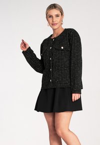 Czarna koszula w kratkę z fakturowanym wykończeniem, wyposażona w dwie kieszenie, zapięcie na guziki i okrągły dekolt, zestawiona z rozkloszowaną czarną spódnicą.