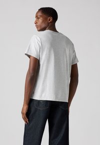 Grijze katoenen T-shirt met een ronde hals, korte mouwen en een losse pasvorm. Opvallend Levi's-logo aan de onderzijde. Gecombineerd met donkere denim broek.