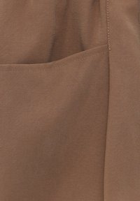 Tissu marron à texture lisse, comportant une poche. Le design est simple, avec des coutures nettes le long des bords.