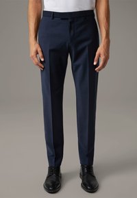 Marineblauwe broek gemaakt van een gladde stof, met een getailleerde pasvorm en een rechte voorkant. Gecombineerd met zwarte dresschoenen, zonder zichtbare patronen of accenten.