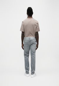 Γκρι τζιν παντελόνι και ανοιχτό καφέ μπλουζάκι. Το τζιν έχει στενή εφαρμογή και πίσω τσέπες, ενώ το μπλουζάκι διαθέτει λαιμόκοψη τύπου crew.