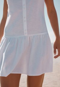 Biele bavlnené šaty do kolien s gombíkovou légou vpredu, nariaseným pásom a rozšírenou sukňou. Hladká textúra s jednoduchým dizajnom.