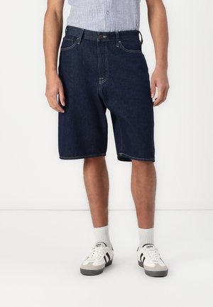 Shorts din denim de culoare bleumarin închis, cu o croială confortabilă, având închidere cu nasture, cinci buzunare și detalii de cusătură subtile. Purtați cu adidași albi.