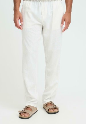 Letvægts hvide linnedbukser med elastisk snøre i taljen og sideslidser. Kombineret med brune ruskindsandaler med spænde.