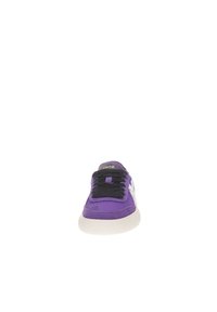 Zapatillas moradas con un upper de tela texturizada, cordones negros y una suela de goma blanca. La lengüeta tiene una etiqueta de logo negra.