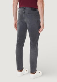 Jeans grigi aderenti con una texture liscia, cinque tasche e un'etichetta con il logo sulla cintura posteriore, abbinati a sneakers bianche.