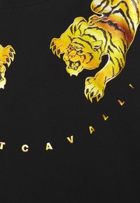 Felpa nera con illustrazioni di tigri dorate lucide e testo metallico che mette in risalto il nome del marchio in un motivo semicircolare.