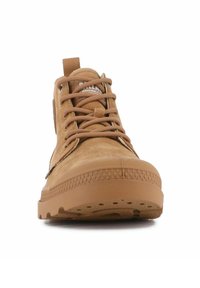 Botas marrones de media caña hechas de ante con suela de goma, puntera redondeada y diseño de cordones. Presentan una lengüeta con tirador y un logo en la parte superior.