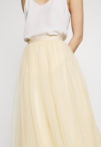 Jupe en tulle jaune pâle avec un intérieur doublé, présentant de délicats motifs à pois blancs et une taille ajustée. Conception légère et fluide.