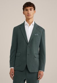 Green textured blazer with notched lapels, single button closure, and two front pockets. Worn over a white shirt, featuring a patterned pocket square.