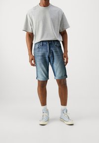 Šedé tričko s krátkým rukávem v kombinaci s vyhrnutými džínovými kraťasy. Světle modré tenisky s bílými podrážkami a kotníkové ponožky doplňují tento outfit.