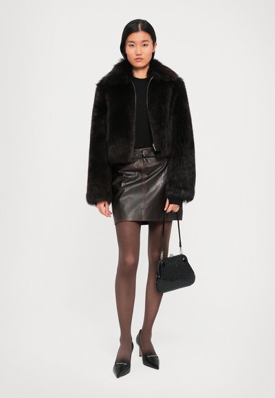 Woman wearing a black faux fur jacket, black top, dark brown leather mini skirt, sheer tights, black heels, and holding a black handbag.