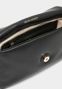 Schwarze Leder-Clutch mit einem goldfarbenen Druckknopfverschluss. Sie verfügt über ein beiges Innenfutter und eine innere Reißverschlusstasche. Logo eingeprägt innen.