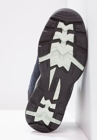 Trail-Schuh mit einem strukturierten, dunkelgrauen Obermaterial, Gummilaufsohle mit einem Zickzack-Profil in hellgrün und verstärktem Fersenbereich.