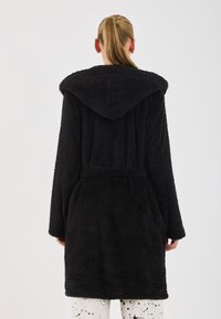 Rochie neagră, pufoasă, cu glugă, având un cordon la talie, mâneci lungi și o textură moale. Cusăturile sunt vizibile pe margini.