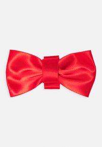 Laço de cetim vermelho com um nó central, apresentando uma textura suave e forma simétrica, medindo aproximadamente 15 centímetros de largura.