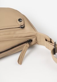 Beige leather bag with a triangular shape, featuring two zippered pockets and contrasting black hardware. Smooth texture with visible stitching.