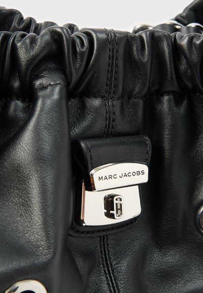 Κοντινό πλάνο μαύρης δερμάτινης τσάντας χειρός με μαζεμένο πάνω μέρος και ασημένιο κούμπωμα με χαραγμένο το λογότυπο Marc Jacobs.