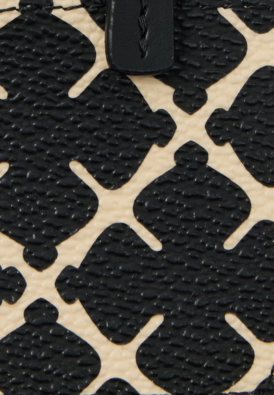 Lähedalt vaadatuna must ja beež tekstuuriga nahk, millel on geomeetriline muster ja väike must õmmeldud nahkdetail. 